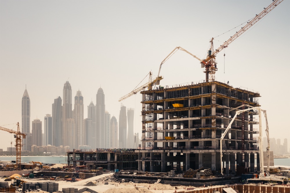 High-rise construction site on the Gulf coast, with the Dubai Marina skyline behind