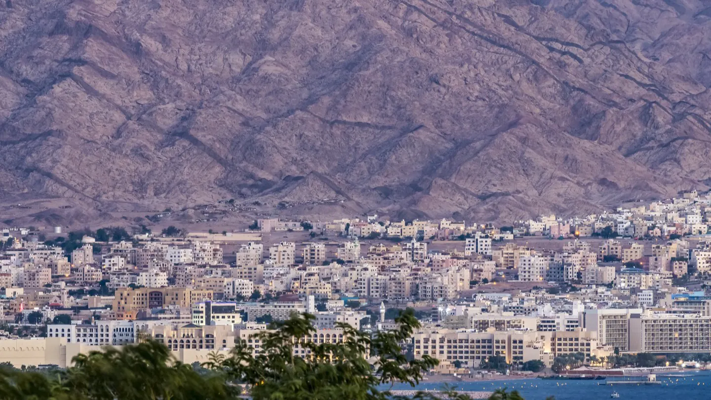 A Red Sea port city at dusk, ringed by arid mountains where the desert meets the water